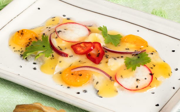 Plate of gourmet ceviche with radish, cherry tomatoes, and herbs, part of 10-course underground dining experience.