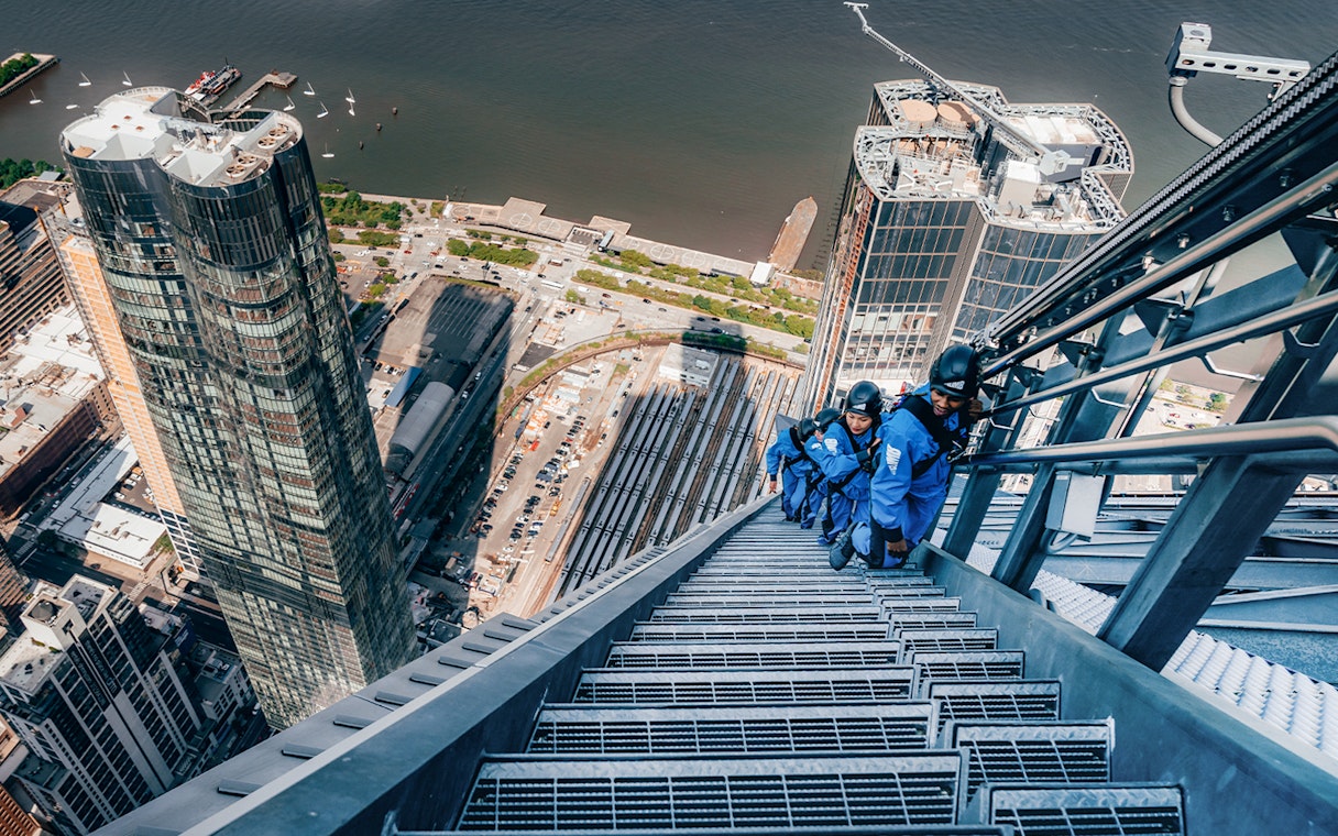 Climbers ascending a skyscraper in Sydney with cityscape and harbor views.