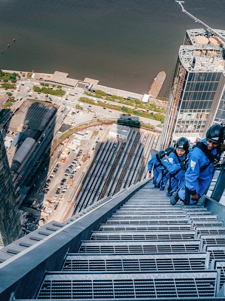 Climbers ascending a skyscraper in Sydney with cityscape and harbor views.