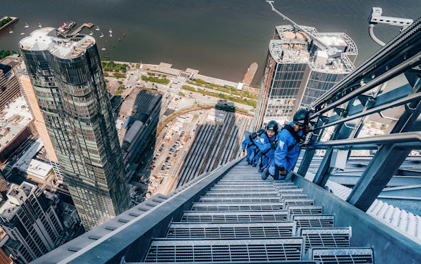 Climbers ascending a skyscraper in Sydney with cityscape and harbor views.