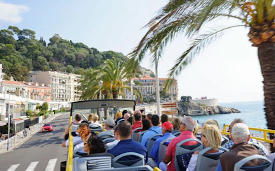 Open-top bus tour along Nice coastline with palm trees and sea view.