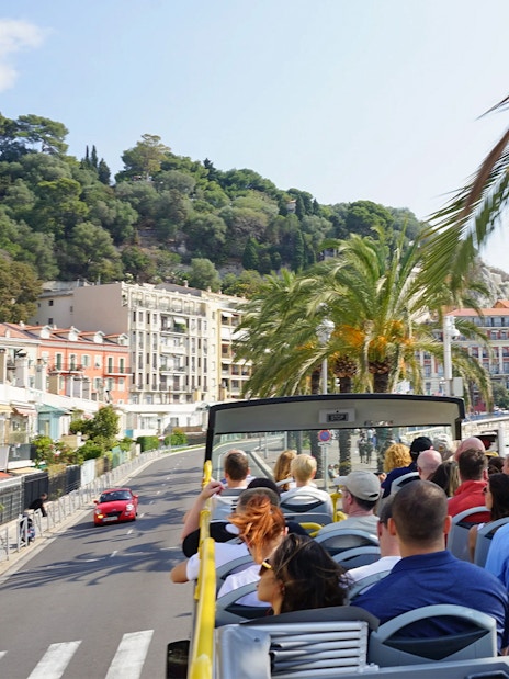 Open-top bus tour along Nice coastline with palm trees and sea view.