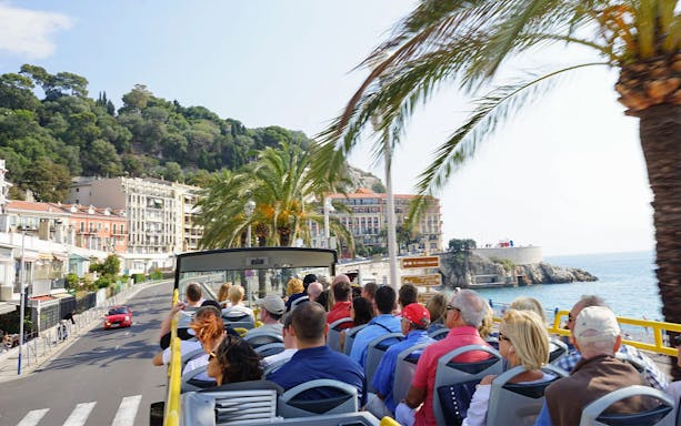 Open-top bus tour along Nice coastline with palm trees and sea view.