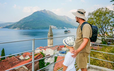 Father and son on rooftop overlooking Kotor Bay and church tower in Perast, Montenegro.