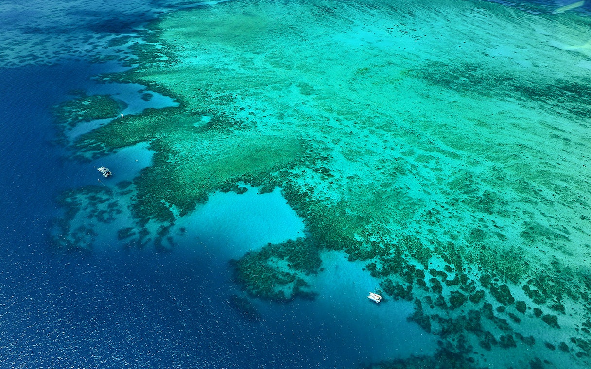 Aerial view of the Great Barrier Reef's outer edges with boats on turquoise waters.