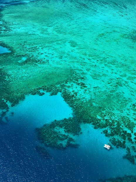 Aerial view of the Great Barrier Reef's outer edges with boats on turquoise waters.