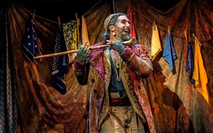 Performer in colorful costume holding a cane on stage during Oliver! musical.