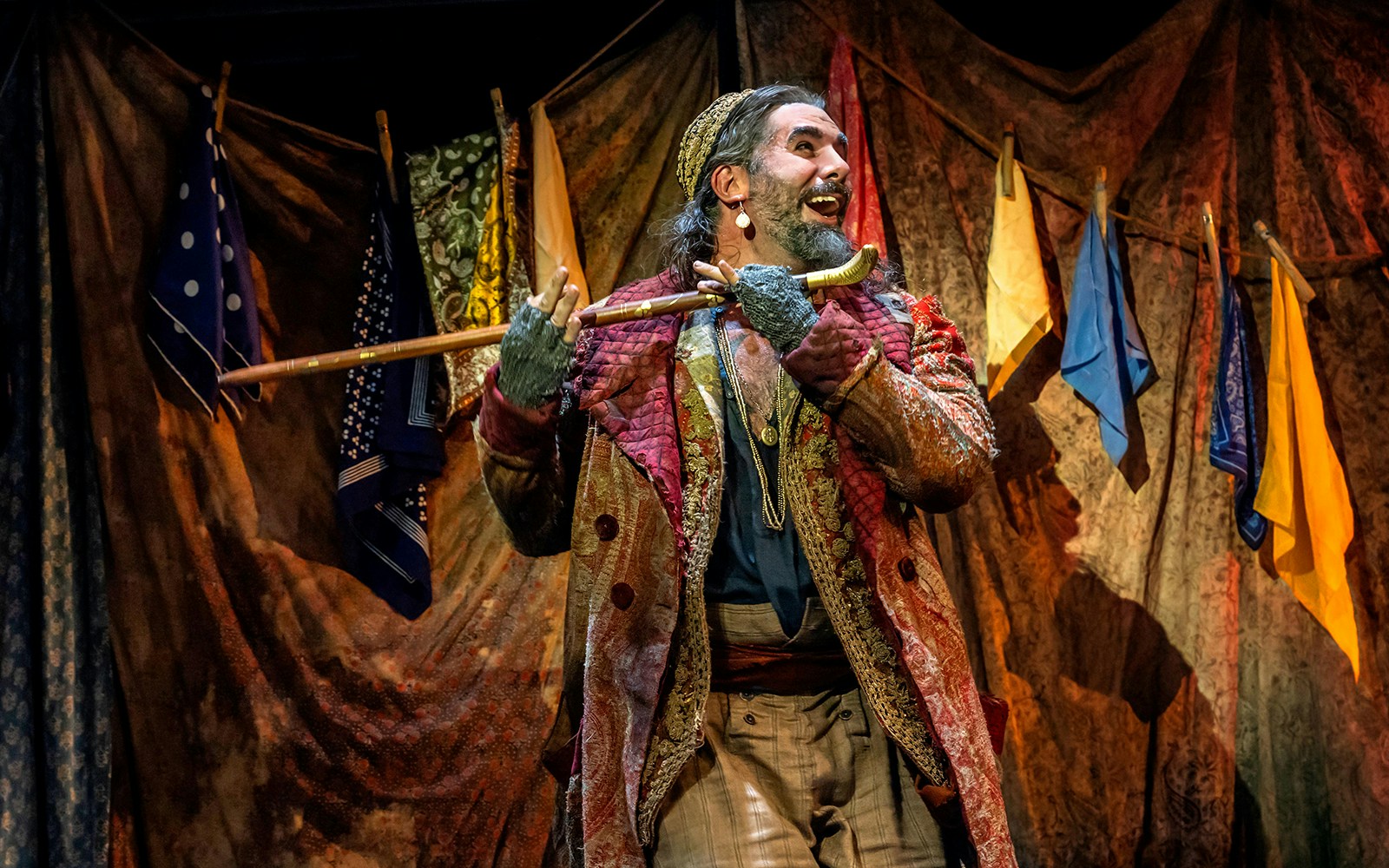 Performer in colorful costume holding a cane on stage during Oliver! musical.