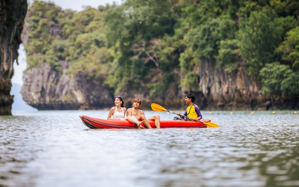 Local paddler guiding canoe on serene river in lush tropical landscape, Vietnam.