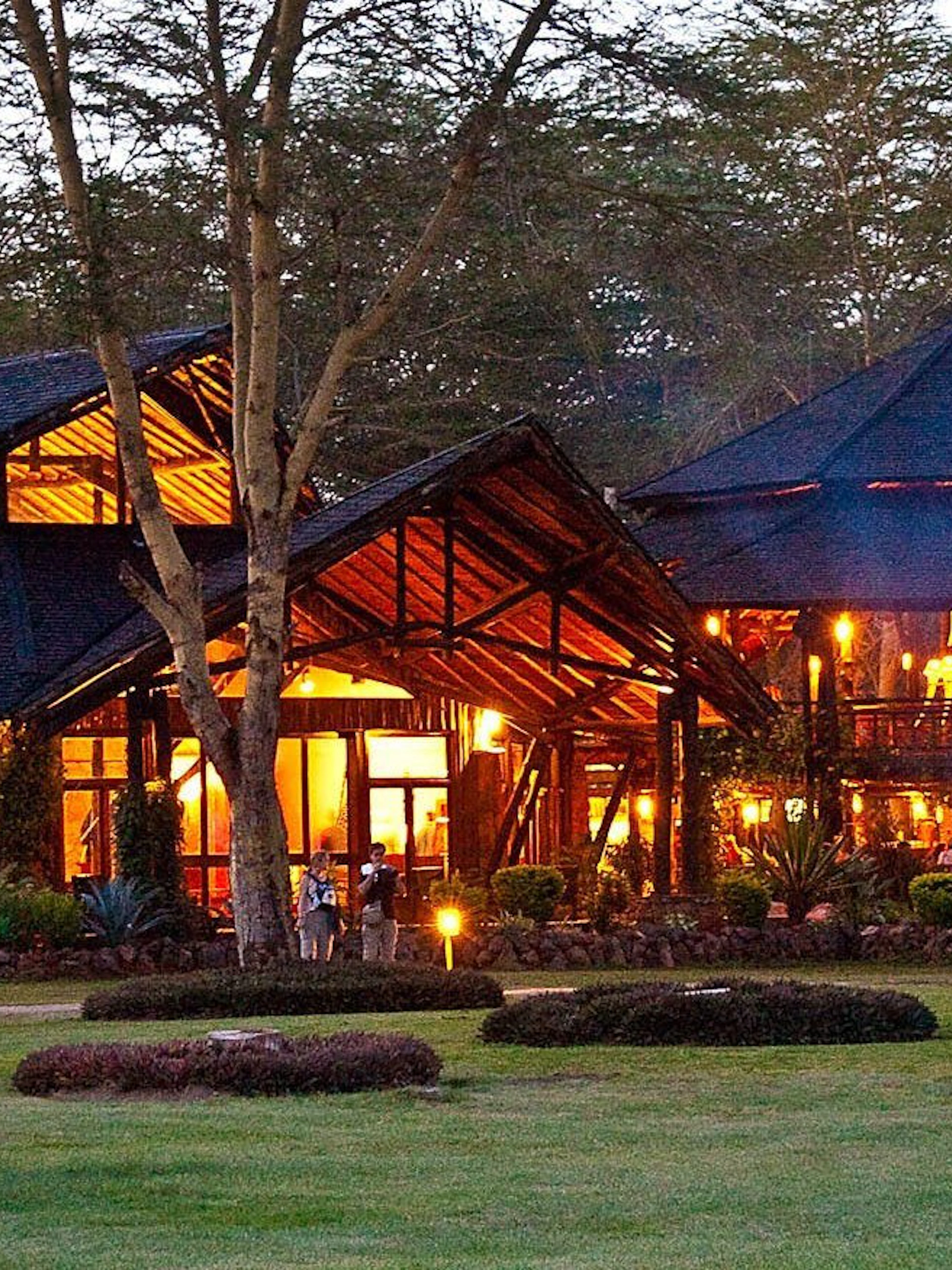 Lodge illuminated at dusk in Amboseli & Tsavo Safari, surrounded by trees and greenery.