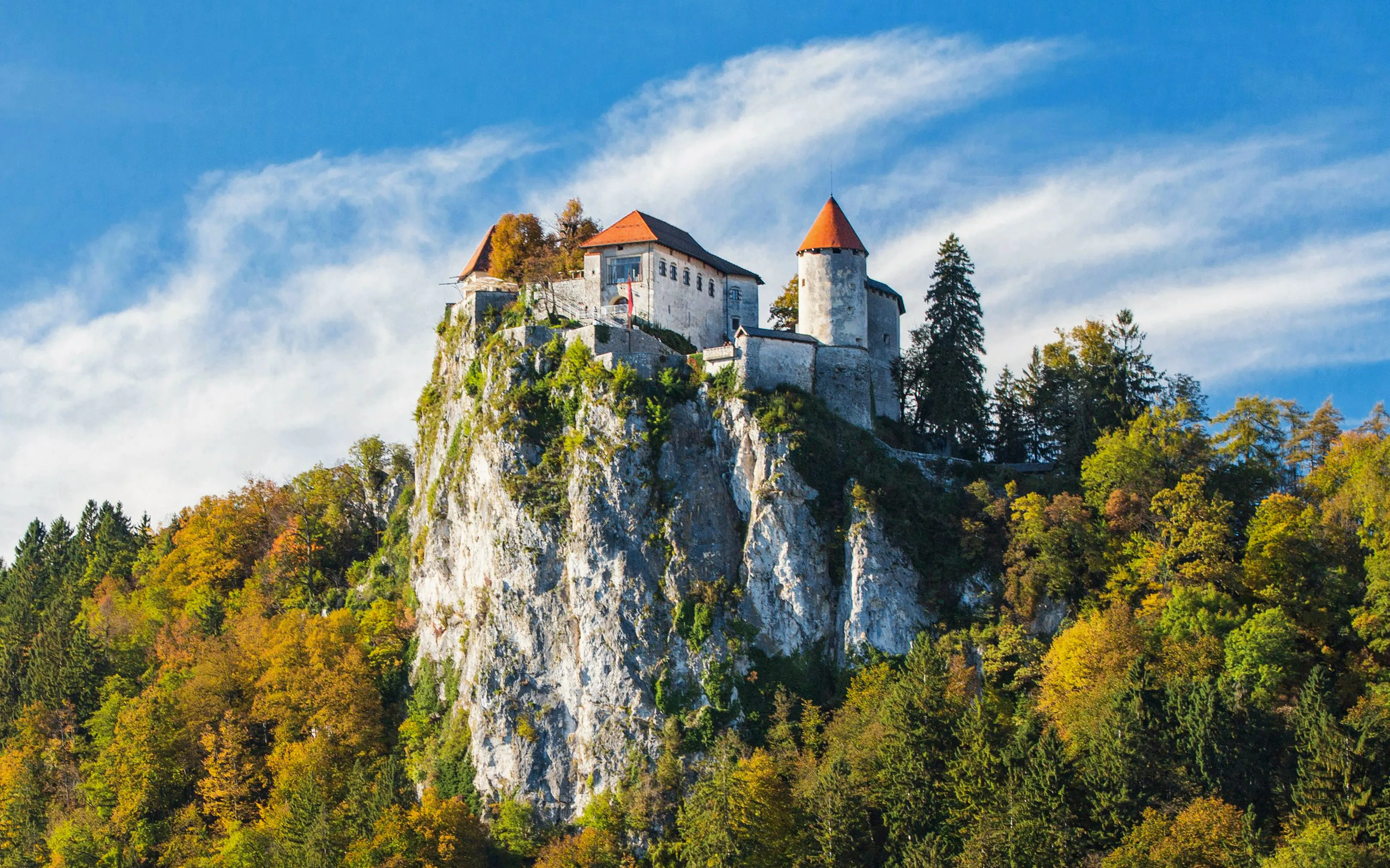 Castle on a rocky cliff surrounded by autumn trees at Lake Bled, Slovenia.