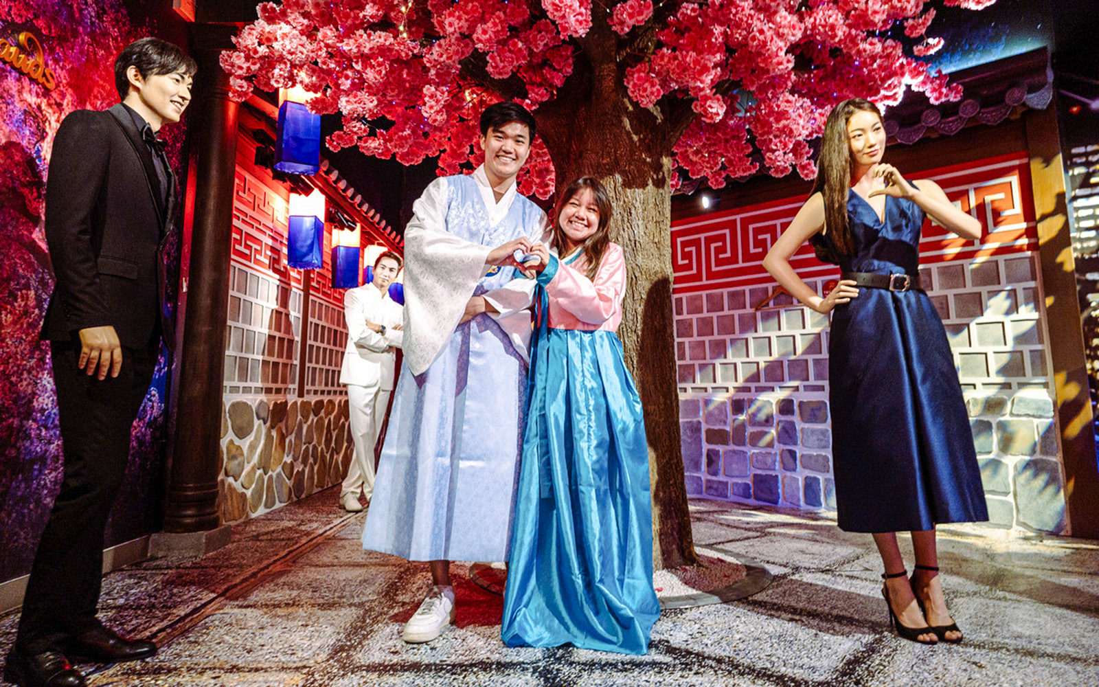 Couple posing in traditional attire at Madame Tussauds Singapore under cherry blossoms.