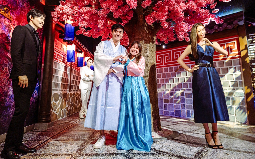 Couple posing in traditional attire at Madame Tussauds Singapore under cherry blossoms.