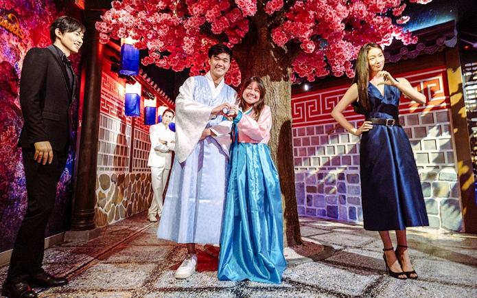 Couple posing in traditional attire at Madame Tussauds Singapore under cherry blossoms.