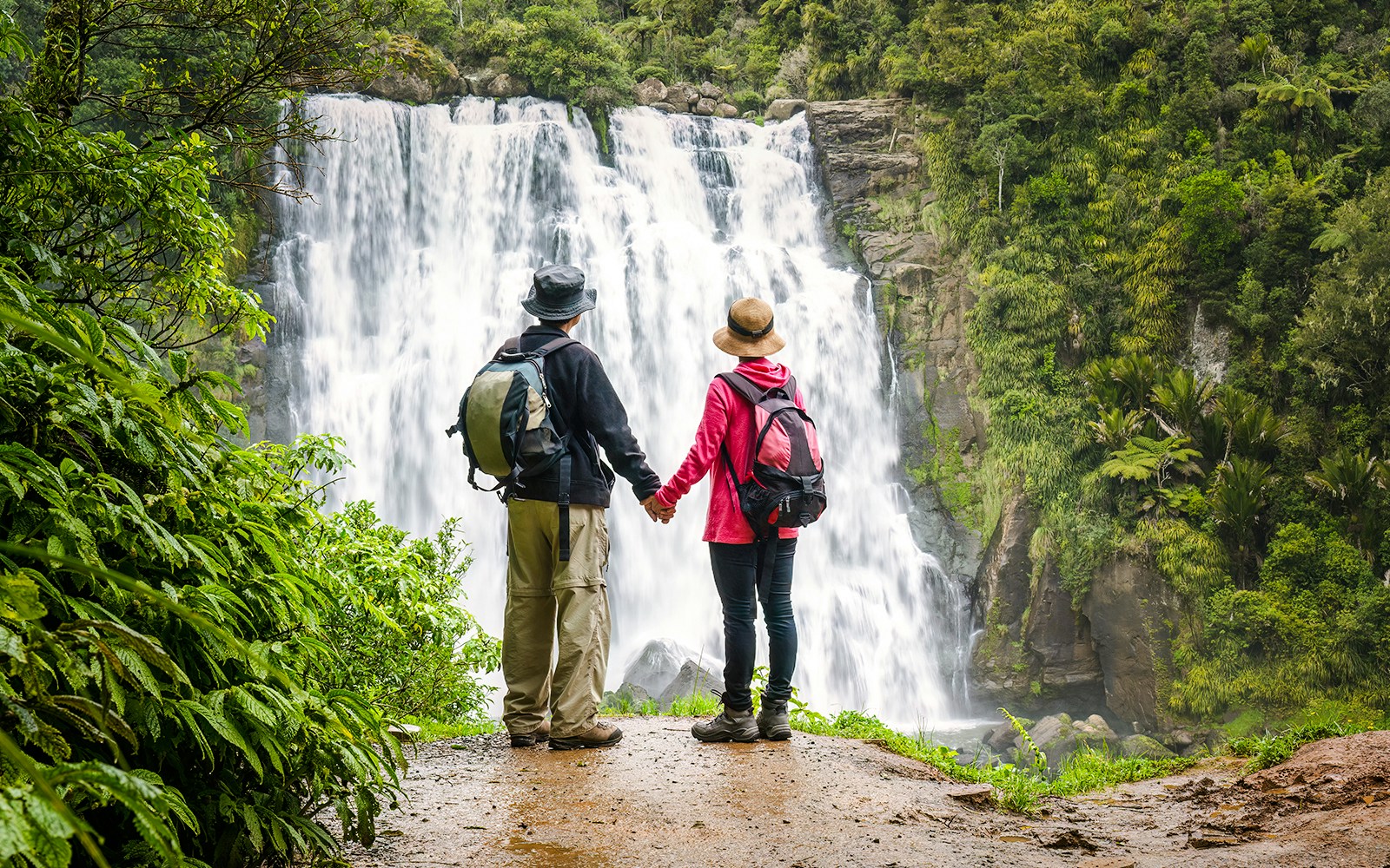 Couple holding hands in front of a waterfall in Waikato, New Zealand.