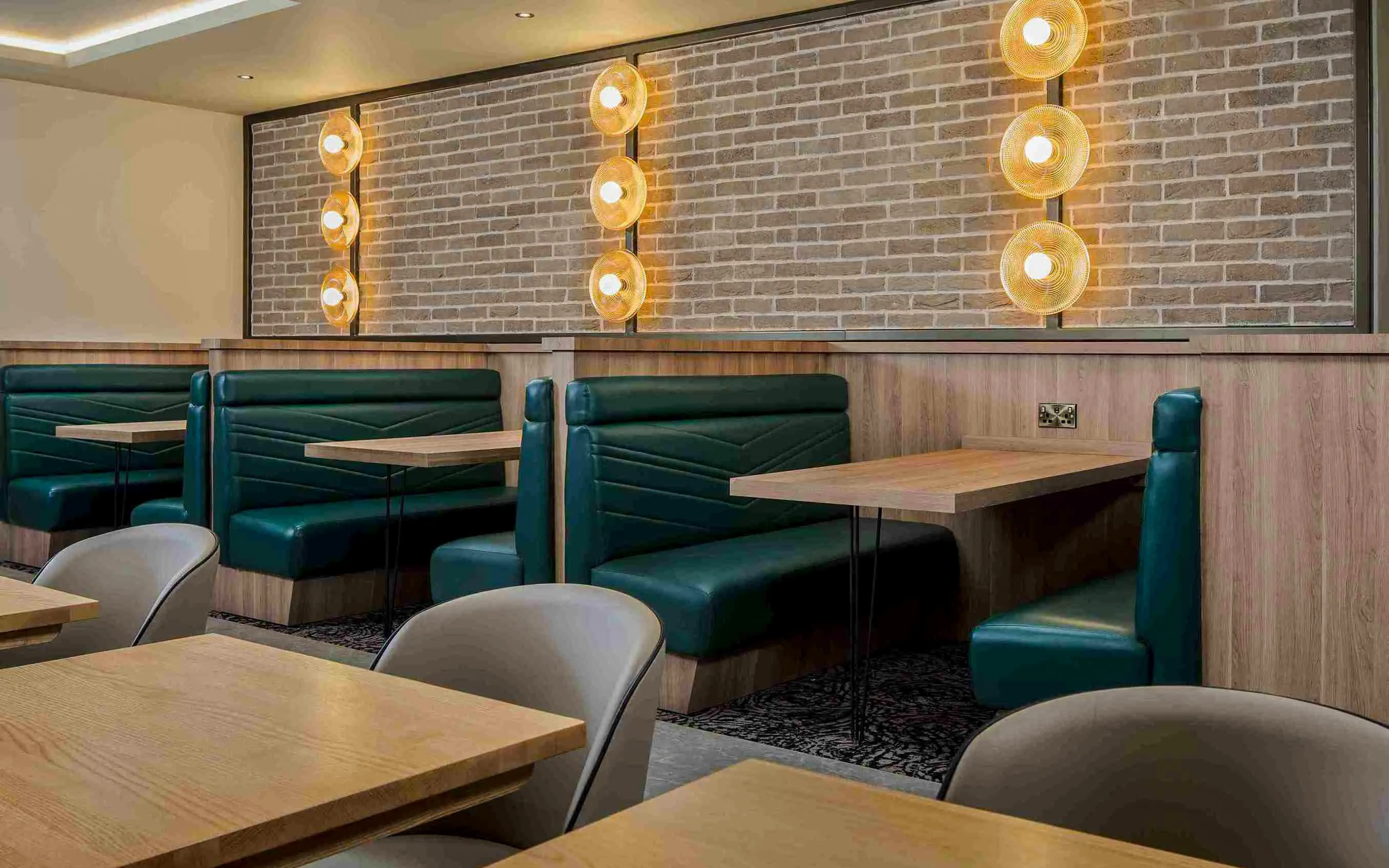 Seating area with green booths and wooden tables at Aspire Lounge, John Lennon Airport.