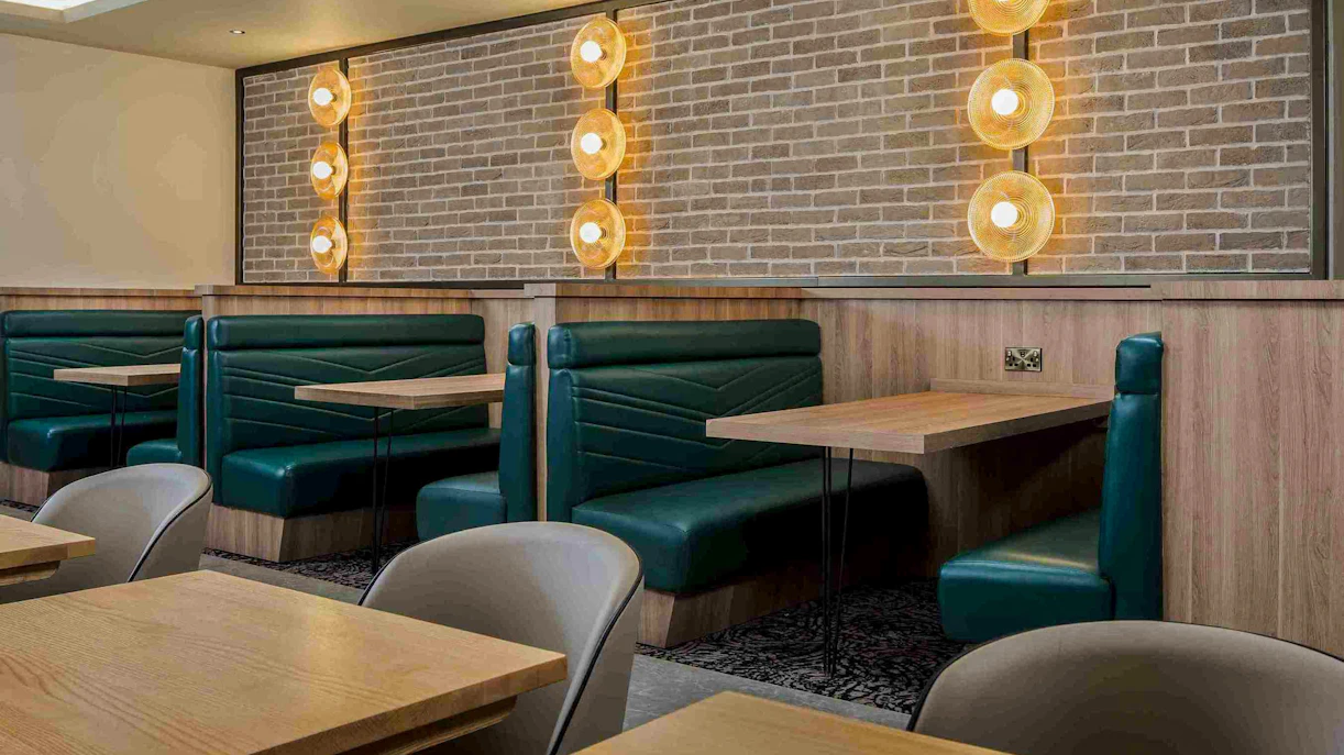 Seating area with green booths and wooden tables at Aspire Lounge, John Lennon Airport.
