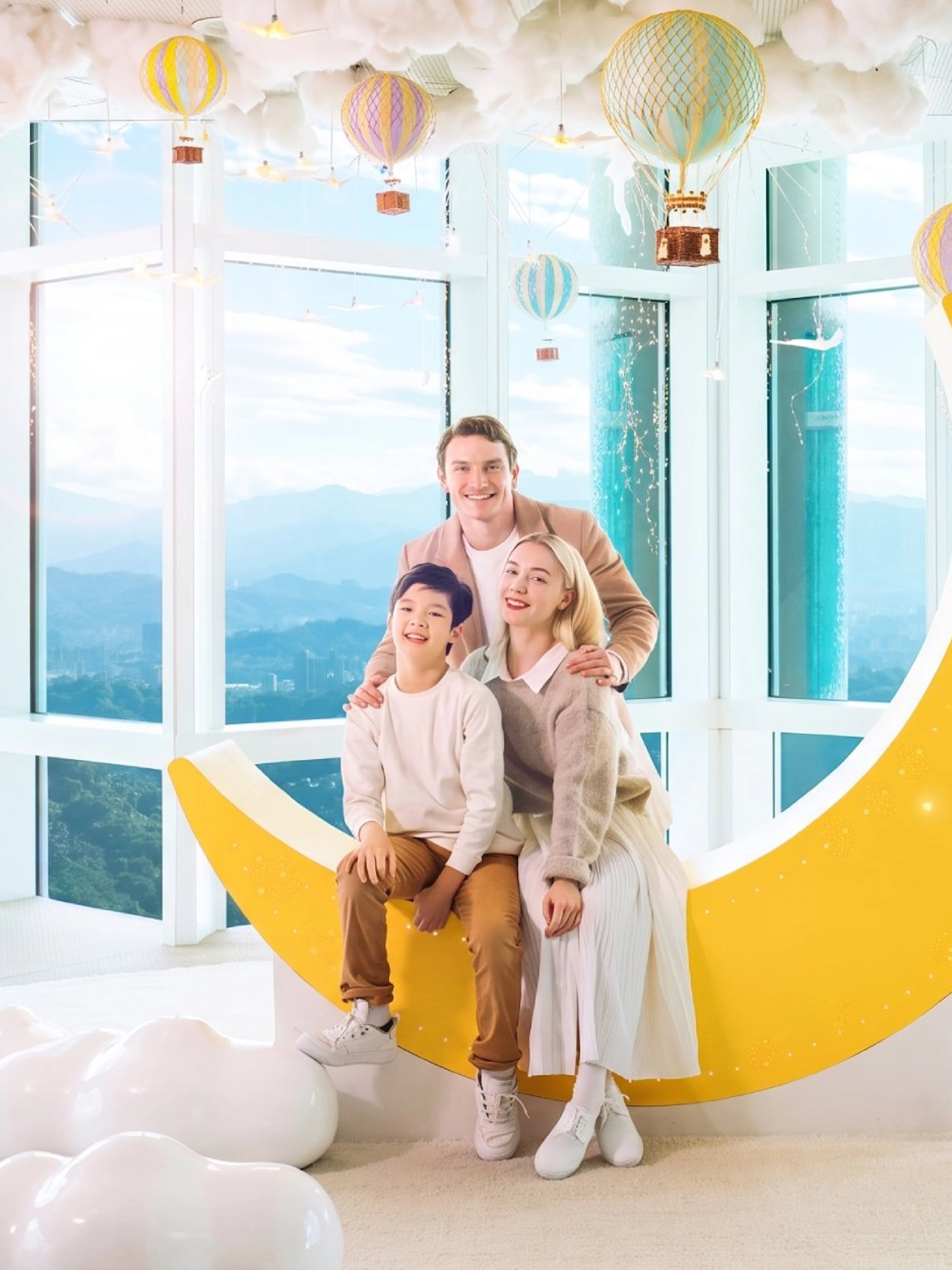 Family posing on a crescent moon sculpture at Taipei 101 Observatory with city view.