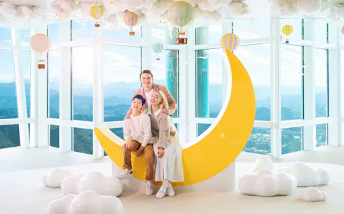 Family posing on a crescent moon sculpture at Taipei 101 Observatory with city view.