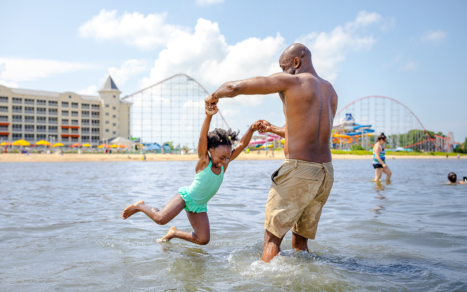 Father and daughter playing in the water at Cedar Point lake with roller coasters in the background.
