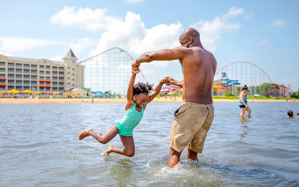 Father and daughter playing in the water at Cedar Point lake with roller coasters in the background.