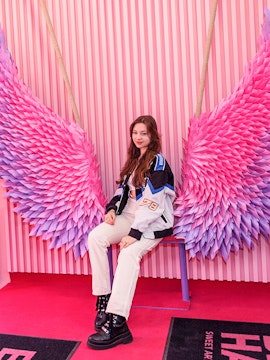 Person sitting on a bench with pink and purple wings at Be Happy Museum, Krakow.