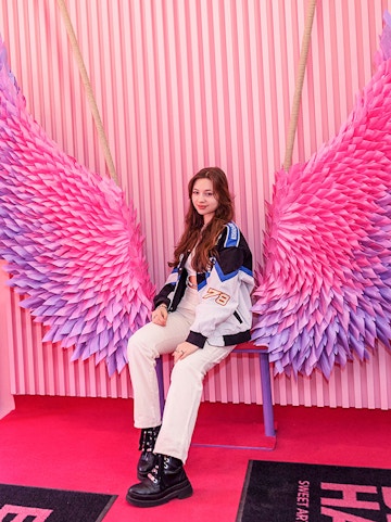 Person sitting on a bench with pink and purple wings at Be Happy Museum, Krakow.
