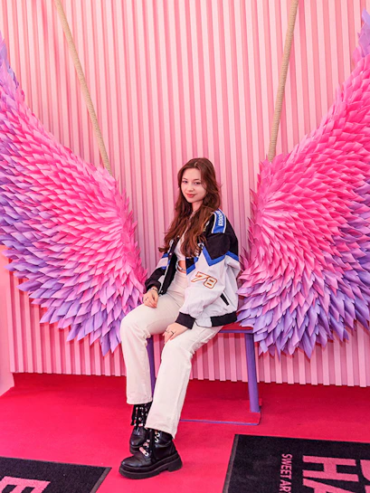 Person sitting on a bench with pink and purple wings at Be Happy Museum, Krakow.