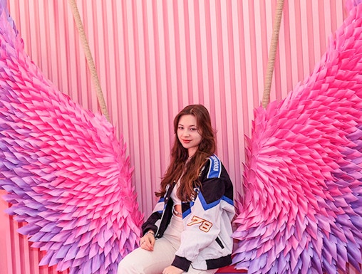 Person sitting on a bench with pink and purple wings at Be Happy Museum, Krakow.