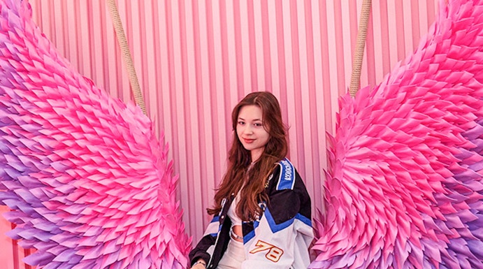 Person sitting on a bench with pink and purple wings at Be Happy Museum, Krakow.