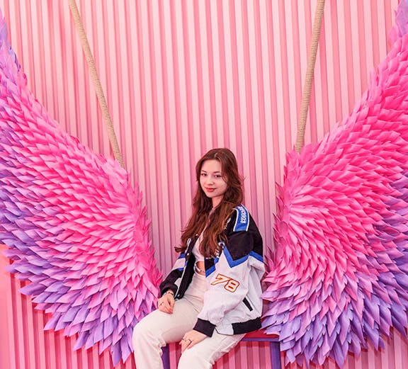 Person sitting on a bench with pink and purple wings at Be Happy Museum, Krakow.