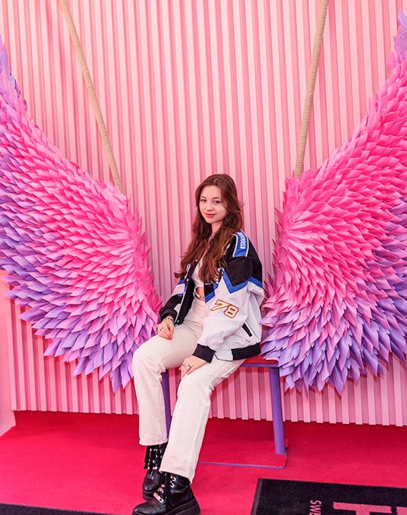 Person sitting on a bench with pink and purple wings at Be Happy Museum, Krakow.