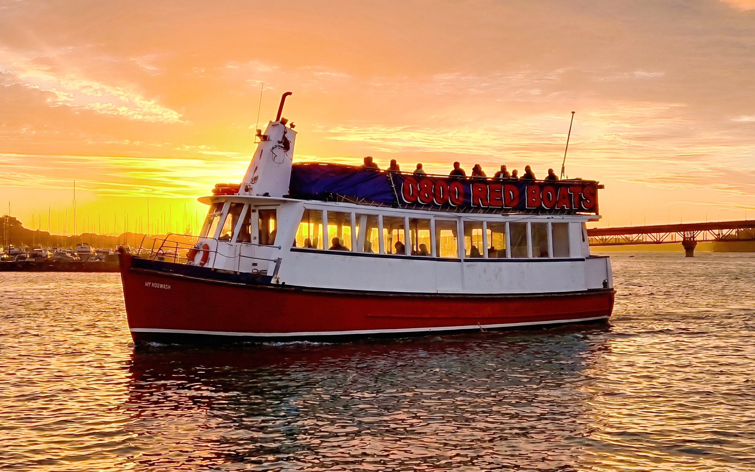 Auckland Harbour cruise boat at sunset with city skyline in background.