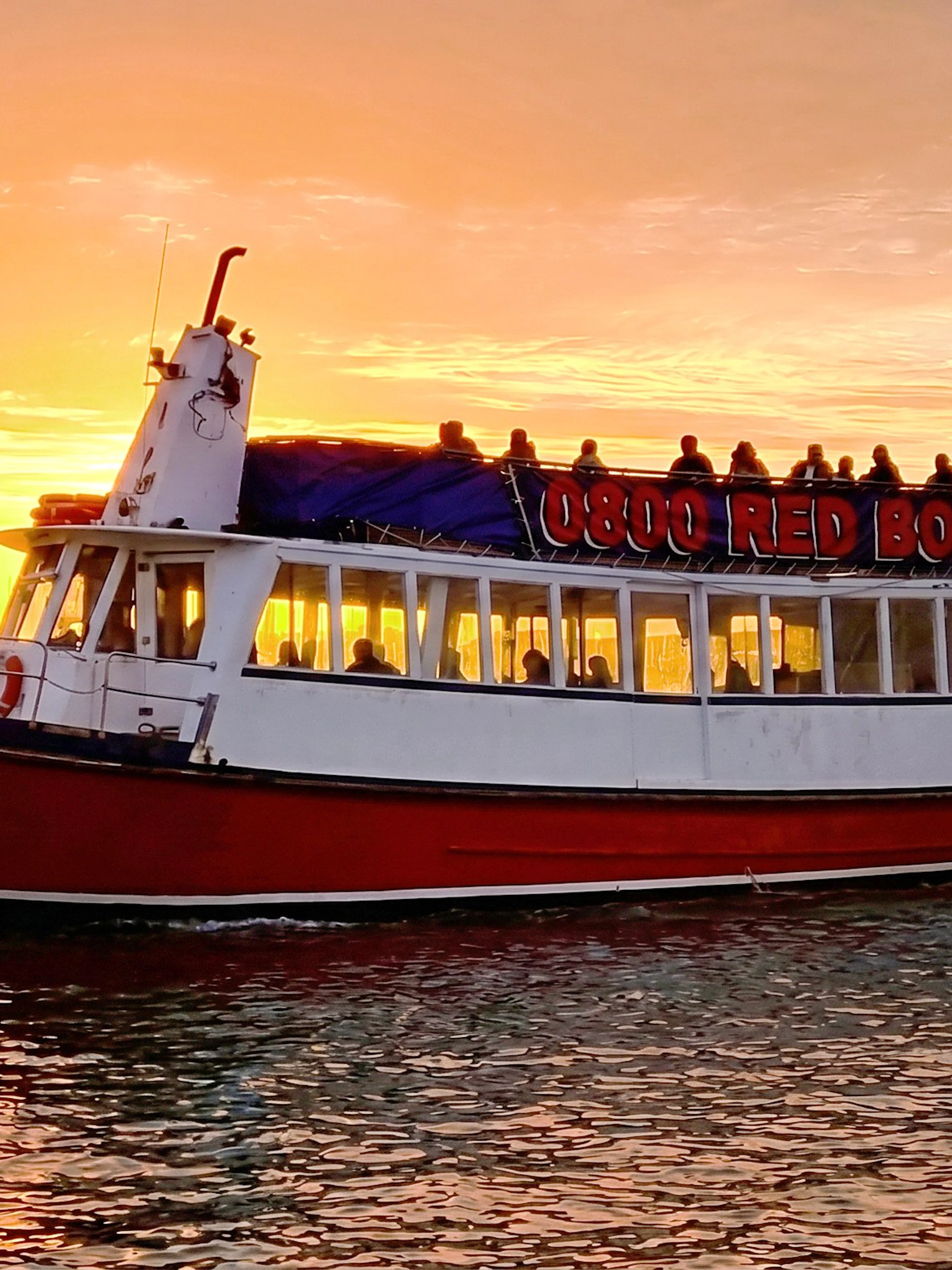 Auckland Harbour cruise boat at sunset with city skyline in background.