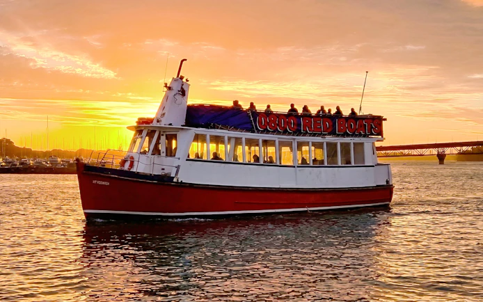 Auckland Harbour cruise boat at sunset with city skyline in background.