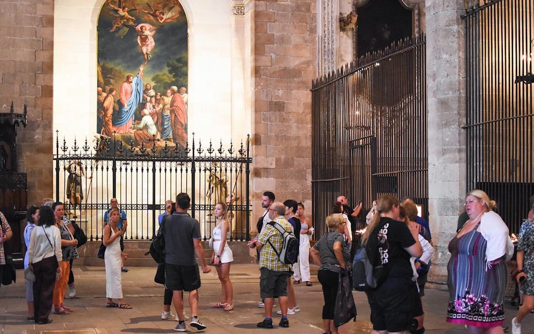 Tourists exploring the interior of Palma Cathedral, Mallorca, with a religious painting in the background.