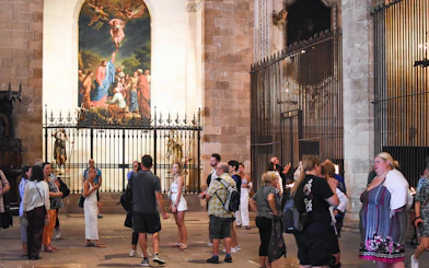 Tourists exploring the interior of Palma Cathedral, Mallorca, with a religious painting in the background.