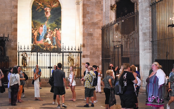 Tourists exploring the interior of Palma Cathedral, Mallorca, with a religious painting in the background.