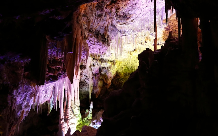 Stalactites and stalagmites inside Drach Caves, Mallorca, illuminated with colorful lights.