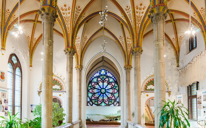 Interior of Vajdahunyad Castle in Budapest with stained glass window and ornate arches.