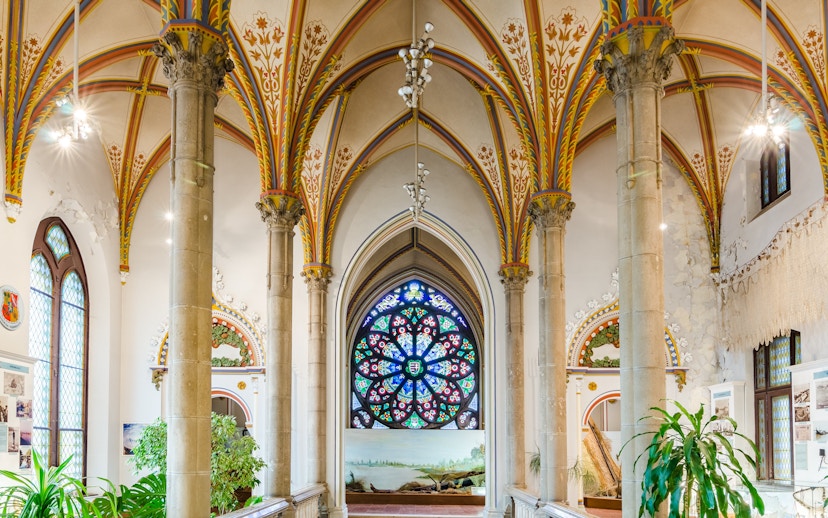 Interior of Vajdahunyad Castle in Budapest with stained glass window and ornate arches.