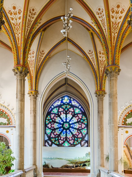 Interior of Vajdahunyad Castle in Budapest with stained glass window and ornate arches.