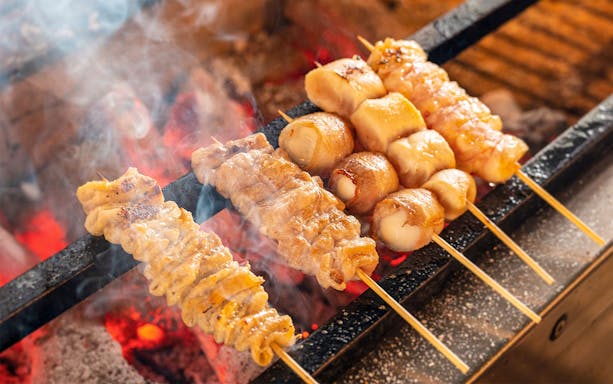 Grilled skewers cooking over charcoal on an Osaka night food tour.
