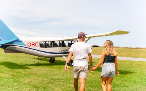Couple walking towards Kaikoura flight on grassy airfield.