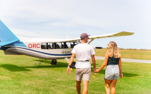 Couple walking towards Kaikoura flight on grassy airfield.