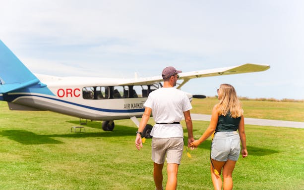 Couple walking towards Kaikoura flight on grassy airfield.