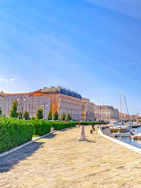 Trieste waterfront promenade with historic buildings and boats by the Adriatic Sea, Italy.