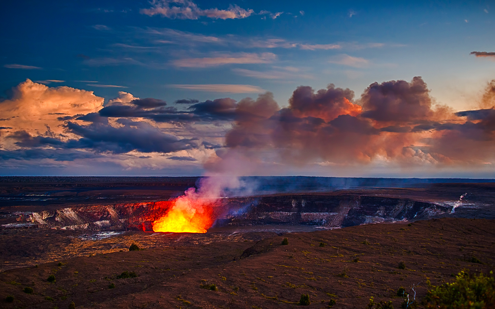 Kilauea Volcano erupting with lava and smoke under a colorful sky in Hawaii.