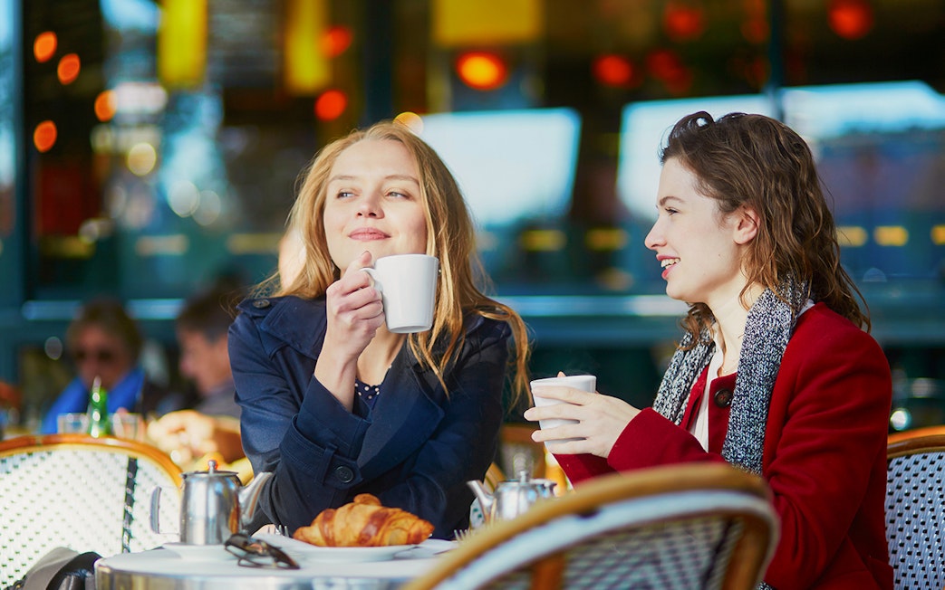 Two young girls enjoying coffee at a cafe table with croissants.