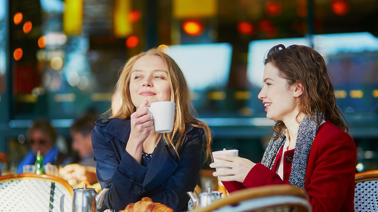 Two young girls enjoying coffee at a cafe table with croissants.